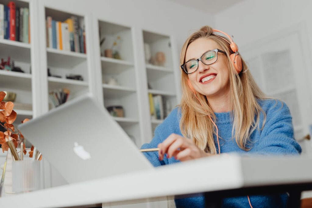 Smiling woman wearing eyeglasses and headphones, working at home on a laptop.